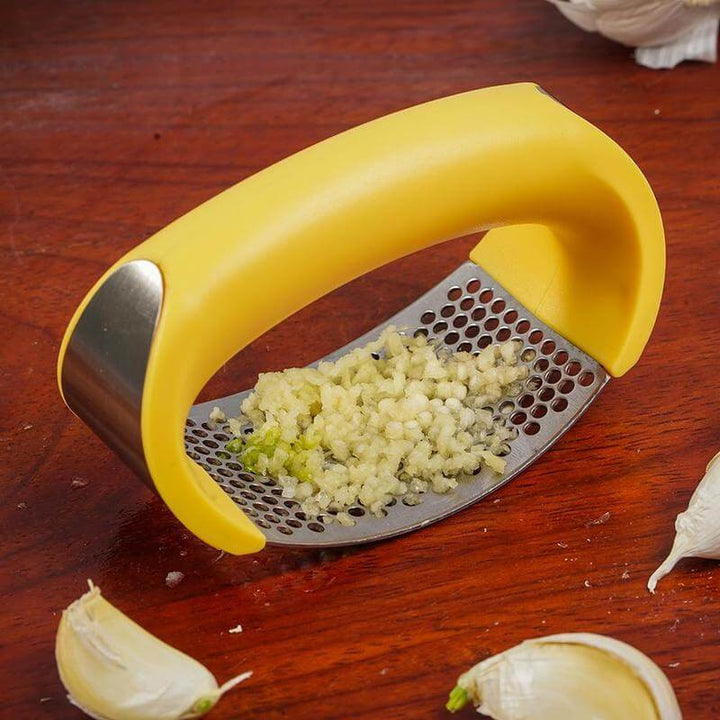 Stainless Steel Garlic Masher with yellow ergonomic handle crushing garlic on wooden surface, easy kitchen tool for quick meal prep.