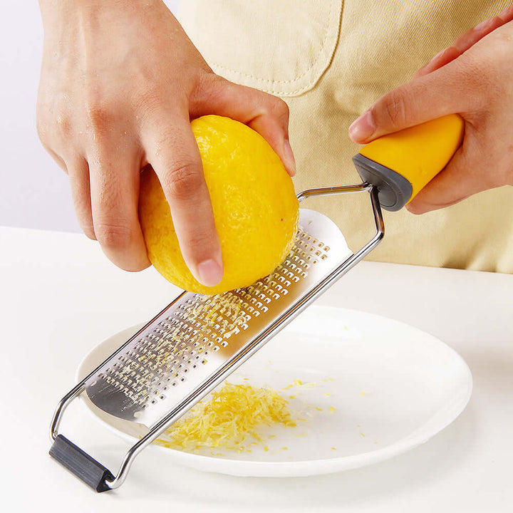 Person using stainless steel cheese grater to zest a lemon over a white plate.