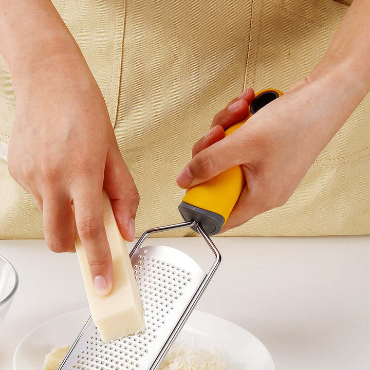 Person using stainless steel cheese grater on block of cheese in kitchen, showcasing durability and multifunctional design.