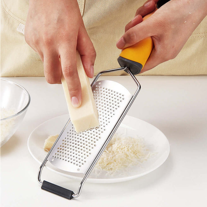 Effortlessly grating cheese with a premium stainless steel mill grater, a durable kitchen tool for slicing and shredding.