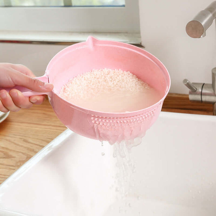 Person rinsing rice in pink strainer over sink in a kitchen setting.