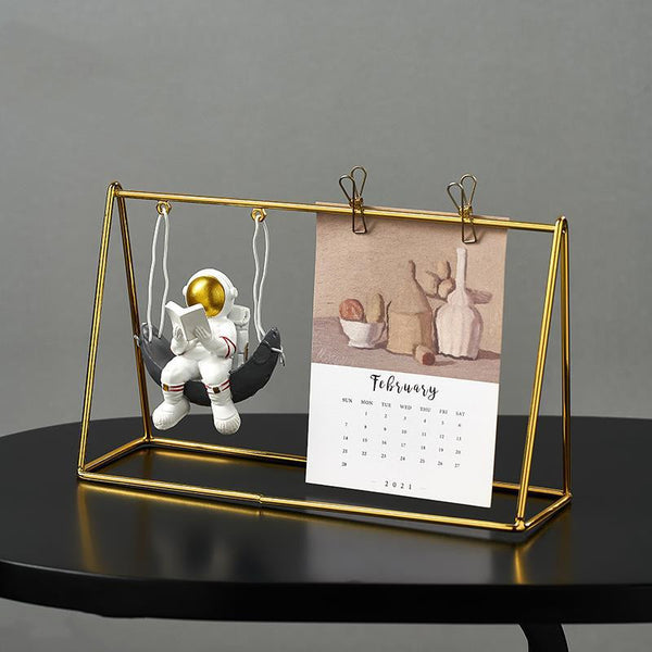 Gold-framed astronaut figurine calendar with swinging spaceman, ideal for space-themed office or living room decor.