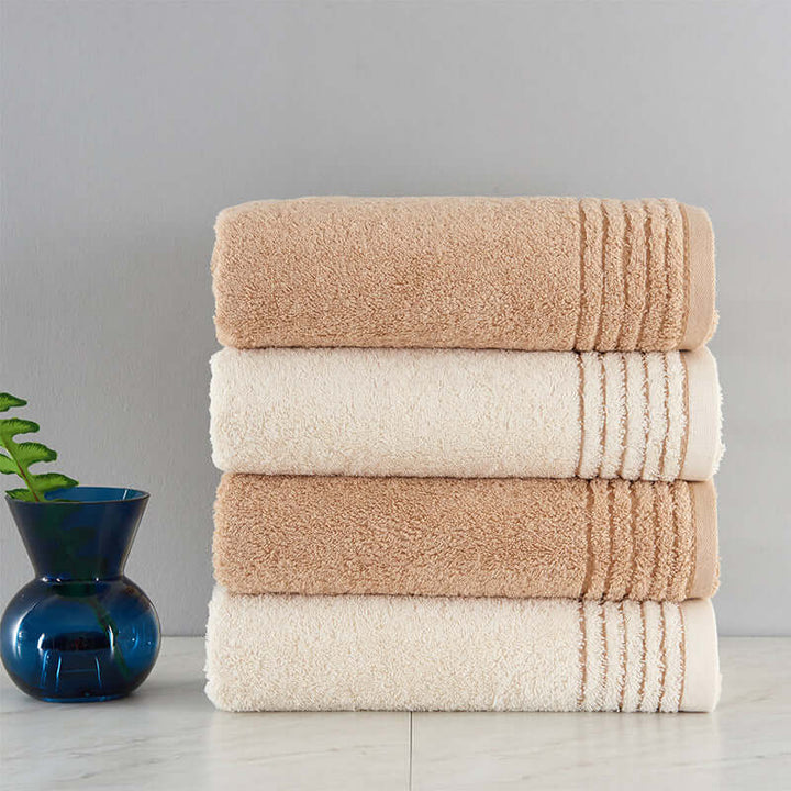 Stack of soft cotton towels in beige and cream, offering luxurious absorbency, ideal for sustainable and cozy home bathroom décor.