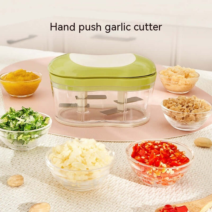 Hand push garlic cutter with chopped vegetables in bowls, displayed on a kitchen counter.