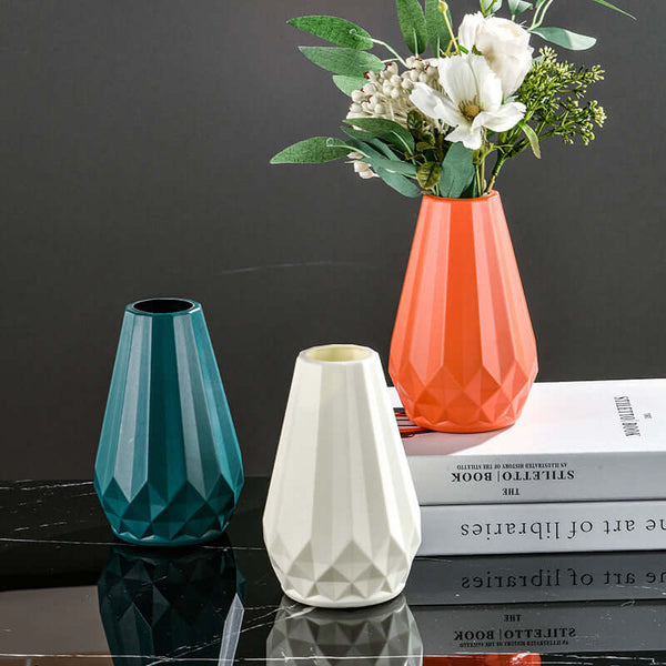 Three Nordic style colorful vases on a table with books and flowers, showcasing vibrant teal, white, and orange shades in a modern design.