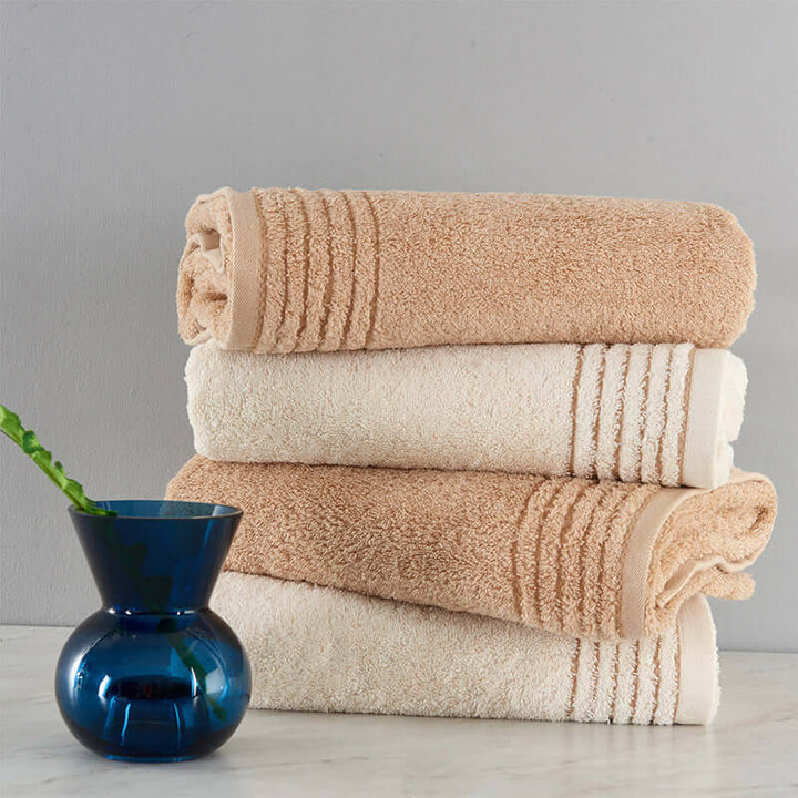 Soft cotton towel set with beige and cream tones next to a blue vase, showcasing luxurious, absorbent bath towels.