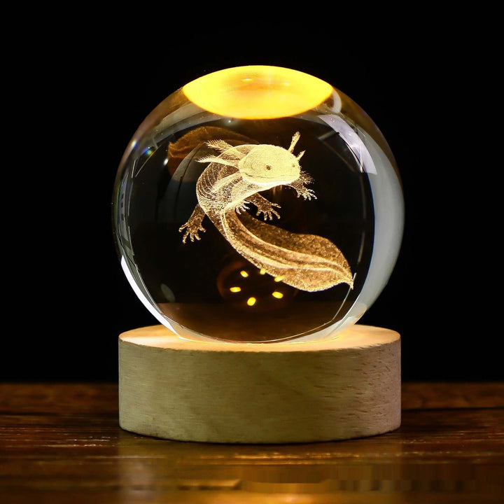 Illuminated crystal ball with axolotl engraving on a wooden base, glowing in dark ambience, perfect for cozy decor.