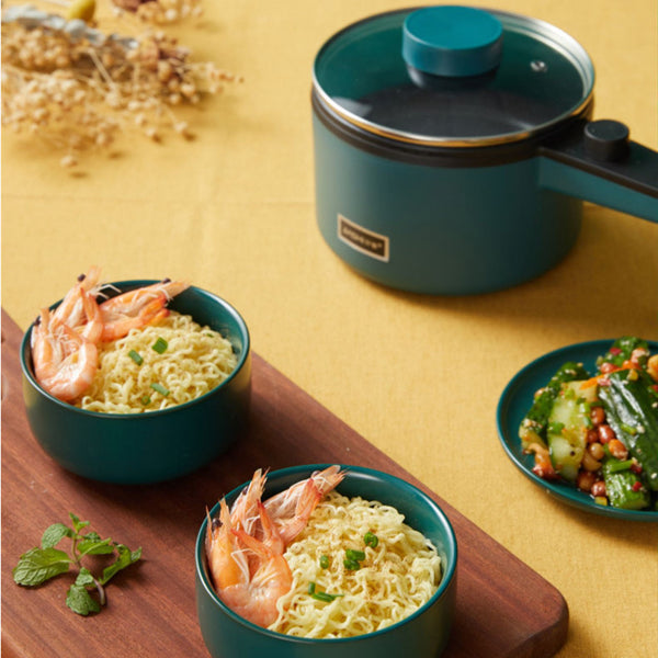 Mini Kitchen Electric Pot with noodles, showcasing multifunctional cooking in a biophilic design, teal color on a wooden board.