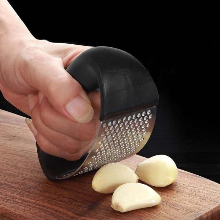 Stainless Steel Garlic Masher in use, crushing garlic cloves on a wooden board.