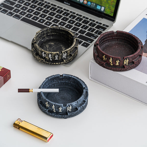 Decorative stone-textured ashtrays in black, red, and blue next to a laptop and lighter, featuring traditional script.