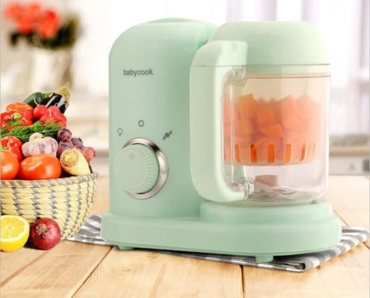 Mint green baby food processor steaming vegetables, surrounded by fresh produce in a cozy kitchen setting.