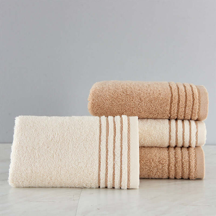 Soft cotton towel set in beige and cream, showcasing biophilic design elements and sustainable materials for a luxurious bathroom feel.