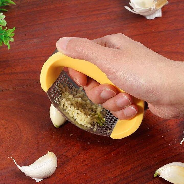 Person using a stainless steel garlic masher to crush garlic on a wooden surface.