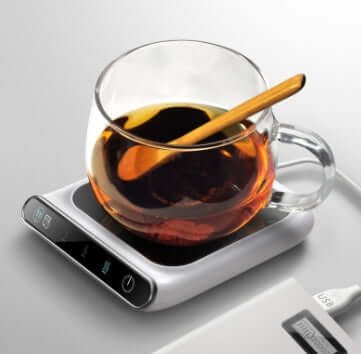 Glass cup on USB-powered mini warmer, keeping tea hot, ideal for cozy spaces with sustainable design. Suitable for office or home use.