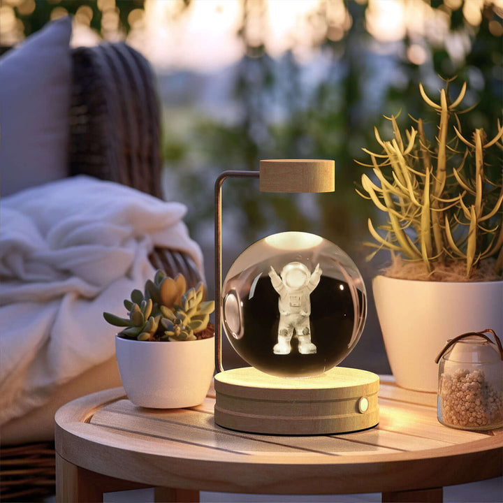 USB-powered Crystal Ball Night Light with 3D design on a wooden table, surrounded by potted plants, for cozy and romantic ambiance.