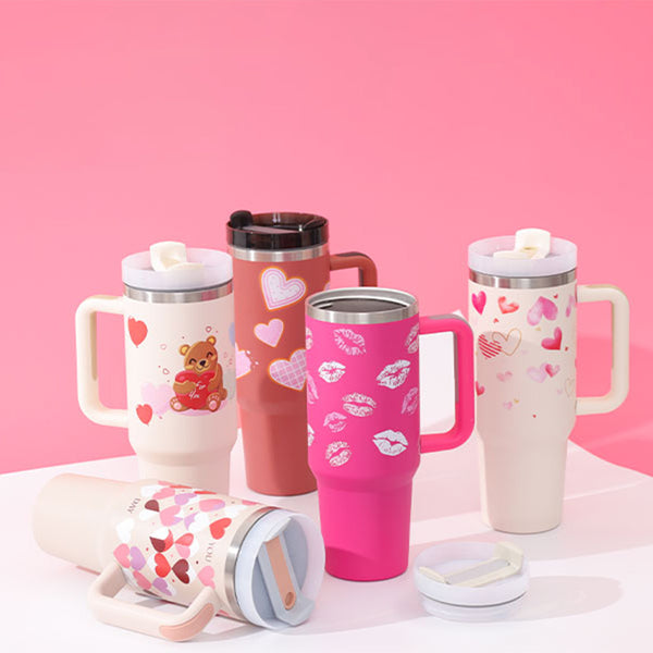 Colorful insulated tumblers with handles and heart designs, perfect for hot and cold beverages, against a pink background.