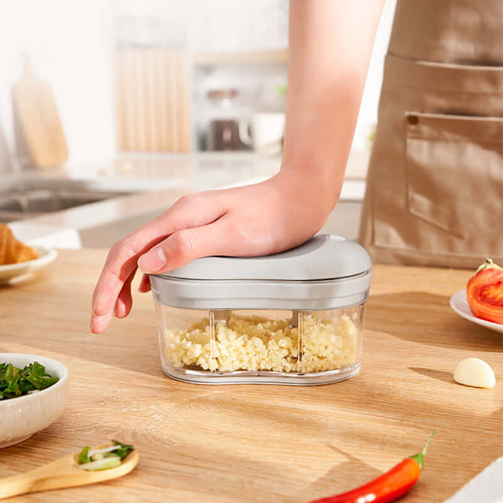 Hand using a gray garlic press on a kitchen counter with chopped garlic inside, emphasizing ease of use and convenience.